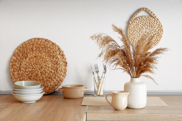 Wicker mat and dishware near white wall on table in kitchen