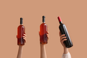 Female hands with bottles of red wine on beige background
