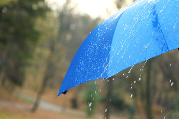Open blue umbrella under pouring rain outdoors, closeup. Space for text