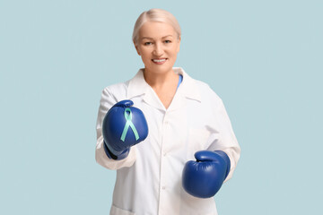 Mature female doctor with boxing gloves and teal ribbon on blue background. Cervical Health...