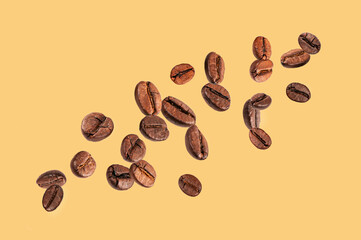 Roasted coffee beans falling on yellow background.