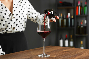 Professional sommelier pouring red wine into glass at wooden table indoors, closeup