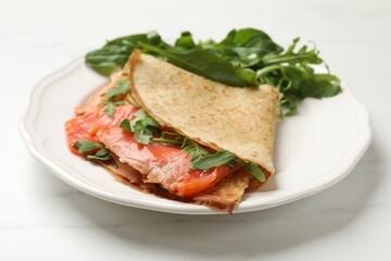 Delicious crepes with salmon and arugula on white table, closeup