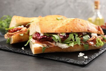 Halves of baguette sandwich with prosciutto and sun dried tomatoes on grey table, closeup