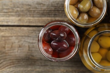 Pickled olives in glass jars on wooden table, flat lay. Space for text