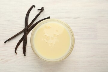 Tasty condensed milk and vanilla pods on white wooden table, flat lay