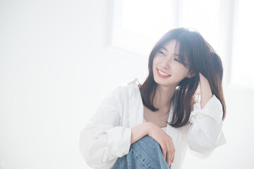 逆光の美しい部屋で髪をかき上げる爽やかな女性　ヘアケアや美容やビューティー　見上げる笑顔