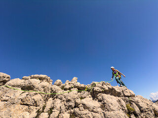 A person is climbing a rock wall with a green rope. The sky is clear and blue, and the person is...