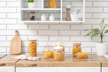 Different jars and bowl with raw pasta shells on table in kitchen