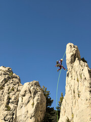 A person is climbing a rock wall with a green rope. The scene is set against a blue sky, creating a sense of adventure and excitement
