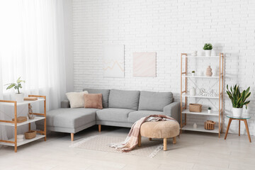 Interior of light living room with grey sofa and shelving units near white brick wall
