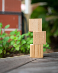 3 blank wooden square blocks stacked on table. Against green nature background.