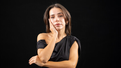 A chest-up headshot of a young, brown-haired woman taken in a studio setting with a black background