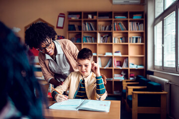 Young Caucasian boy asking for help from his teacher while at the elementary school classroom