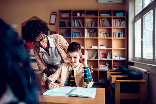 Young Caucasian boy asking for help from his teacher while at the elementary school classroom