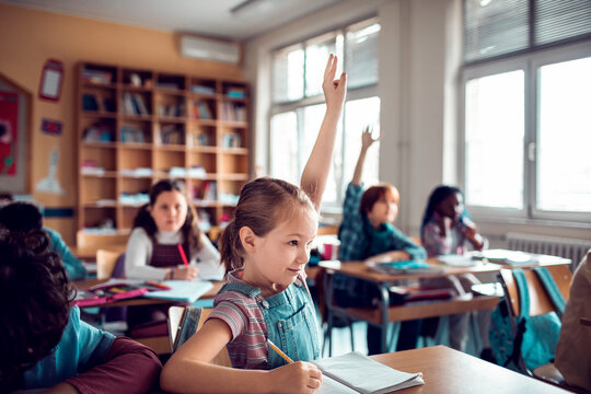 Young Caucasian girl raising her hand for the teacher while at the elementary school classroom