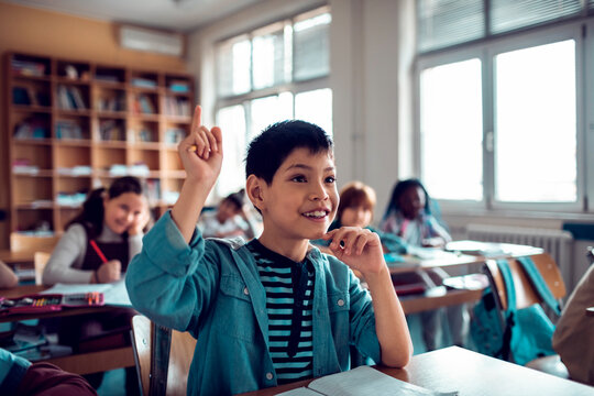 Young Caucasian boy raising his hand for the teacher while at the elementary school classroom