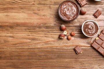 Bowls of sweet chocolate spread and hazelnuts on wooden background