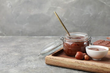 Bowl and jar of sweet chocolate spread with hazelnuts on grey background