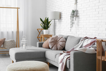 Interior of light living room with sofa, lamp and houseplant near white brick wall