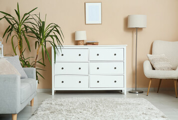 Interior of light living room with chest of drawers, sofa and armchair near beige wall