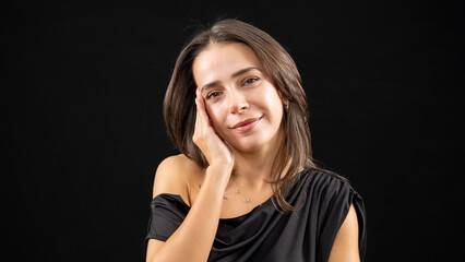 A chest-up headshot of a young, brown-haired woman taken in a studio setting with a black background