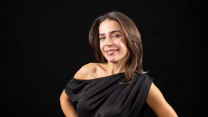A chest-up headshot of a young, brown-haired woman taken in a studio setting with a black background