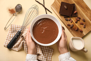 Female hands holding bowl with delicious hot chocolate near whisk and jar of milk on beige background. Top view