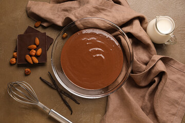 Bowl with hot chocolate, napkin and whisk on brown background. Top view