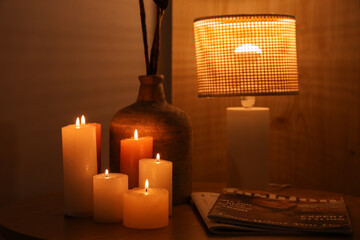Burning candles with vase and glowing lamp on table in bedroom at night