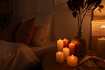 Burning candles and vase with dried flowers on table in bedroom at night