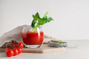 Glass of bloody mary with celery, lime, tomatoes and strainer on light background