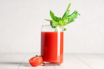 Glass of bloody mary with celery and cut tomato on white tile table