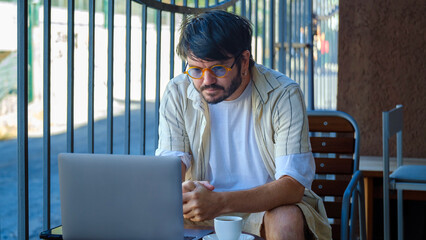A middle-aged businessman is happily working on his laptop in the garden of a café on a summer...