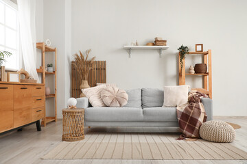 Interior of living room with sofa, pouf and shelving units near white wall