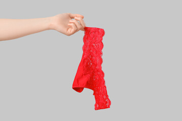 Woman holding red lace panties on grey background