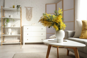Vase with mimosa flowers and magazine on table in living room