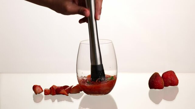 Strawberry mojito cocktail, muddling fresh mint leaves with strawberries to prepare a mojito