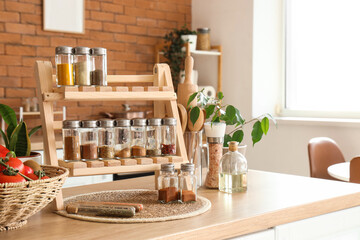 Stand with different spices, utensils and plant on table in kitchen