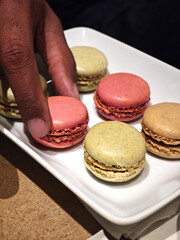 A black man's hand carefully takes a delicious  colorful macarons 