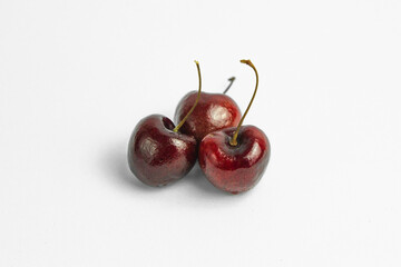 This image shows three dark red cherries against a plain, light background