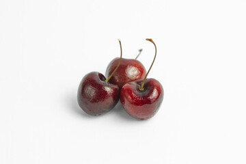 This image shows three dark red cherries against a plain, light background