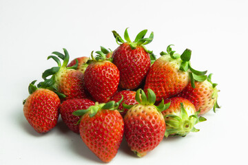 strawberries are arranged in a heart shape on a white background. The berries are red with green stems, some showing a transition to lighter, unripe areas. The image is a top-down view