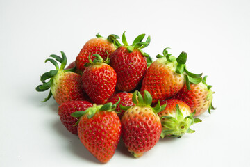strawberries are arranged in a heart shape on a white background. The berries are red with green stems, some showing a transition to lighter, unripe areas. The image is a top-down view