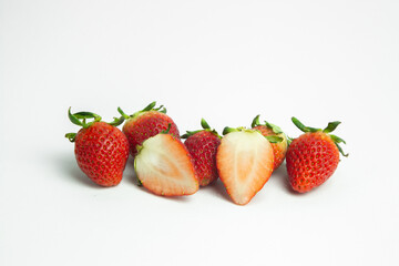 strawberries are arranged in a heart shape on a white background. The berries are red with green stems, some showing a transition to lighter, unripe areas. The image is a top-down view
