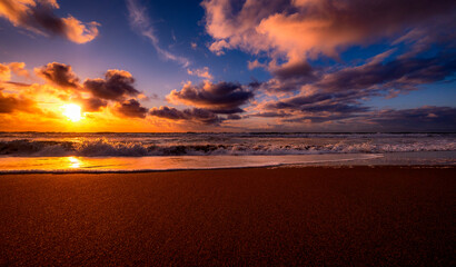 A dramatic sky illuminates with colors of pink and blue casting shades of gold on the ocean and shore during low tide 