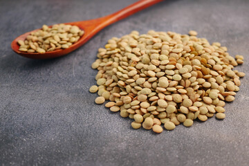 Green lentils scattered next to a wooden spoon on a table