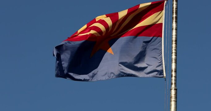 An Arizona State Flag blows in the wind on a blue sky over the the city hall of Jerome, AZ, USA.
