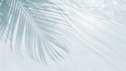 Obraz premium Palm leaf shadow on abstract white sand beach background. Sunlight on water surface, a beautiful abstract background concept banner for summer vacation at the beach. Top view of tropical leaf shadow