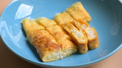 roll omelette stuffed with chesse and rice on blue plate, delicious food in the morning